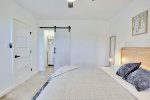 A bedroom with a bed, bedside table, and a door leading to a bathroom. - Hill Country Hideaway Modern Barndominium for 6 (Dripping Springs)