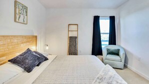 A bedroom with a bed, a chair, a window with curtains, a ceiling fan, and a wall-mounted light fixture. - Hill Country Hideaway Modern Barndominium for 6 (Dripping Springs)
