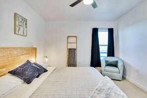 A bedroom with a bed, a chair, a window with curtains, a ceiling fan, and a wall-mounted light fixture. - Hill Country Hideaway Modern Barndominium for 6 (Dripping Springs)