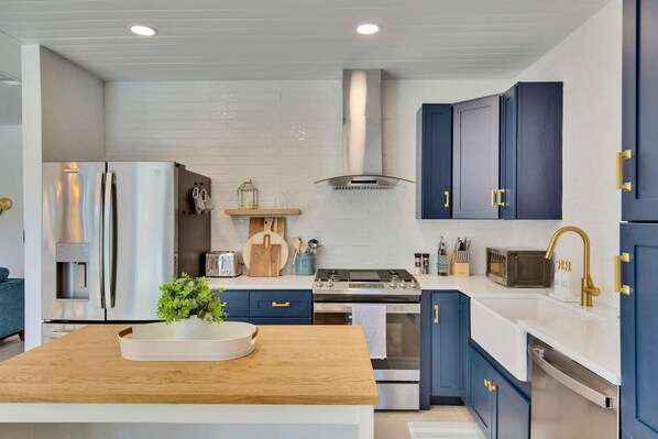 Een moderne keuken met roestvrijstalen apparatuur, een houten aanrechtblad en blauwe kastjes.