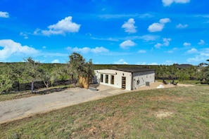 A single-story building with a flat roof, a fenced yard, and a clear sky. - Hill Country Hideaway Modern Barndominium for 6 (Dripping Springs)