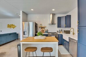 A modern kitchen with a central island, stainless steel appliances, and blue cabinetry. - Hill Country Hideaway Modern Barndominium for 6 (Dripping Springs)
