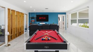 A pool table with balls, a television displaying 'NETFLIX', and a blue wall. - Waterfront Heated Pool Home Gym Fire Pit (Tampa)