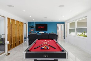 Ein Billardtisch mit Kugeln, ein Fernseher zeigt 'NETFLIX' und eine blaue Wand.