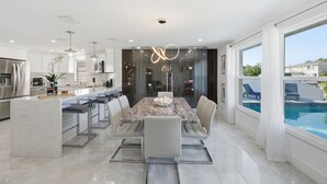 A modern kitchen with a marble island, stainless steel appliances, and a dining area with a marble table and chairs. - Waterfront Heated Pool Home Gym Fire Pit (Tampa)
