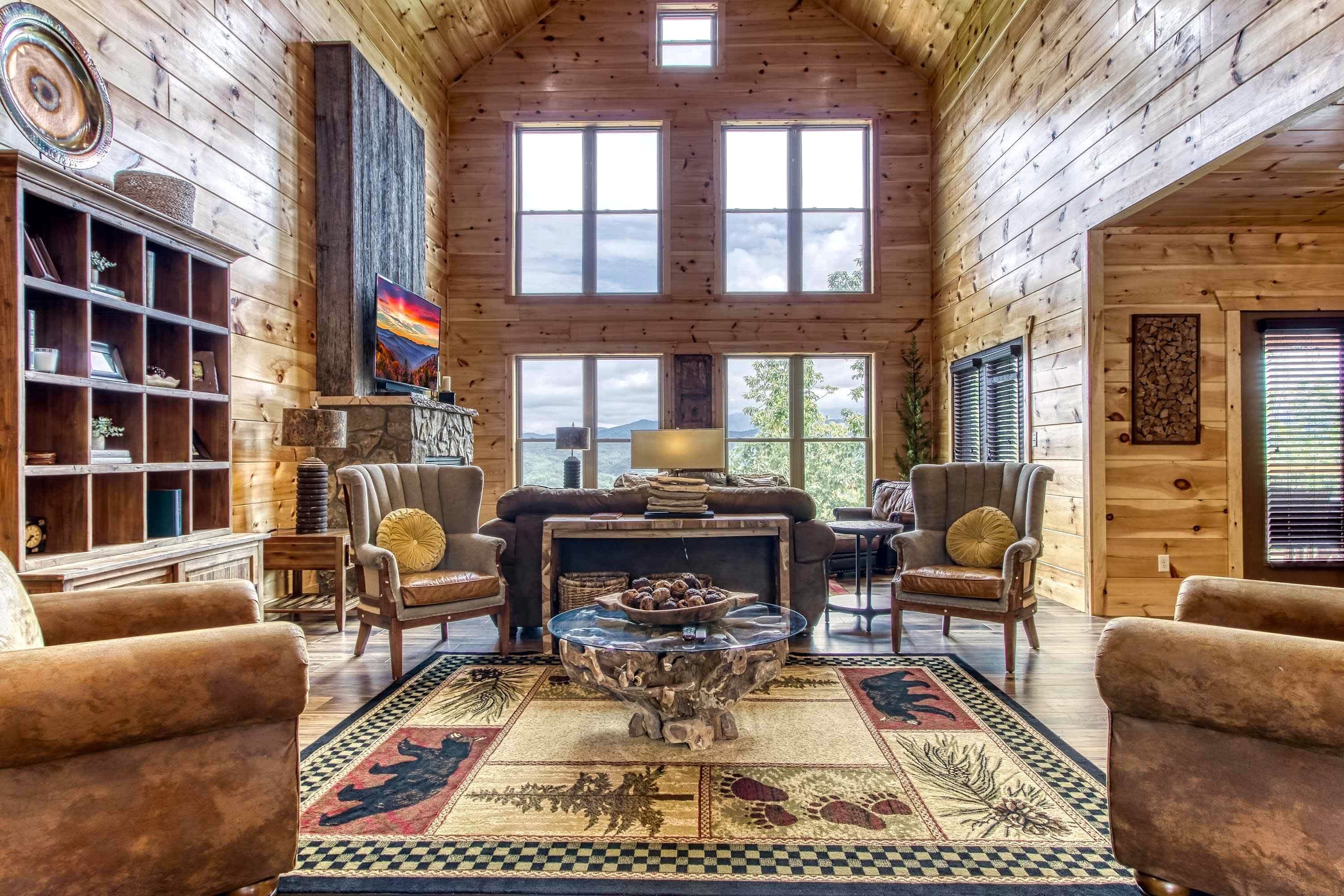 L’intérieur d’une cabane en rondins, avec une cheminée, un coin salon et de grandes fenêtres.