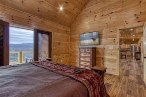 Ein Holzblockhaus-Innenraum mit Bett, Fernseher und Blick ins Freie.