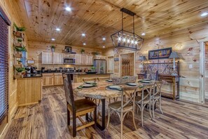 A cabin-style kitchen with wooden cabinets, a dining table set for four, and a hanging light fixture. - Sweet Mimosa Lodge Indoor Pool Hot Tub Views (Sevierville)