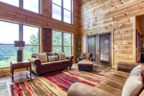 A cozy cabin interior with a large window, a sofa, an ottoman, and a chair. - Sweet Mimosa Lodge Indoor Pool Hot Tub Views (Sevierville)