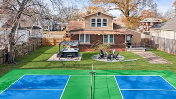 A backyard with a tennis court, hot tub, and outdoor seating area.