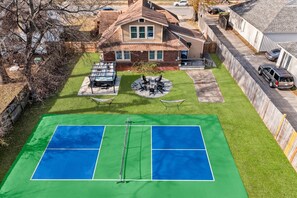 Una propiedad residencial con cancha de tenis, un patio con mobiliario y un garaje.
