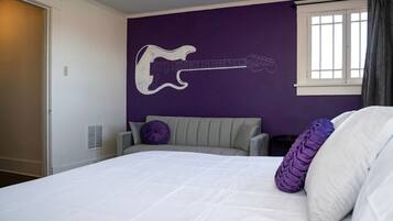 A bedroom with a bed, a grey upholstered headboard, a wall-mounted guitar illustration, a window with curtains, and a white door.