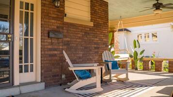 A covered patio with a brick wall, a white door, and a ceiling fan.