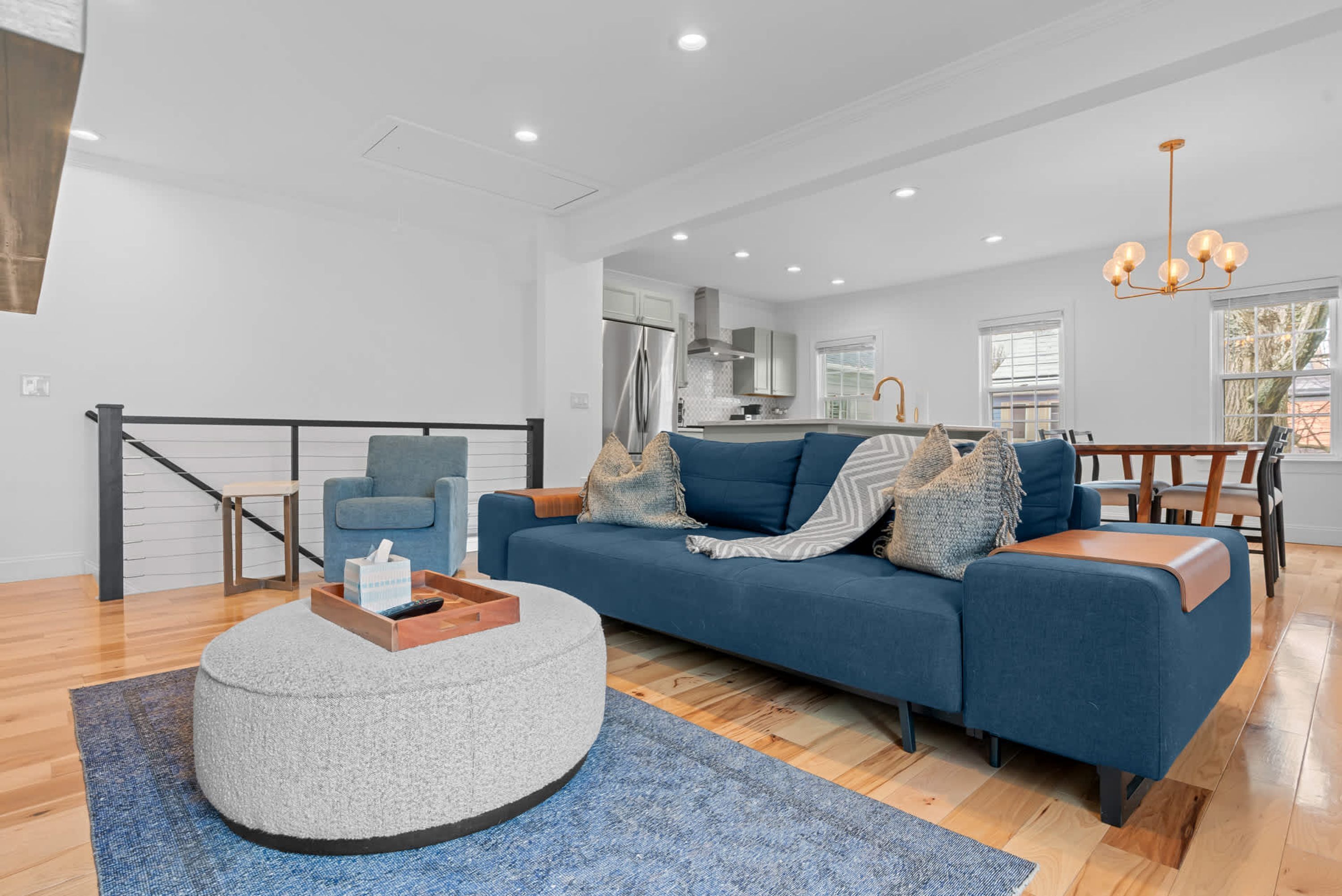 Una sala de estar moderna con un sofá azul, un reposapiés redondo y una mesa de centro de madera.