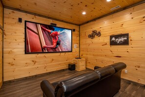 Ein Zimmer mit Holzpaneelen, einem großen Flachbildfernseher an der Wand, einem kleinen Holztisch und einem Ledersofa.