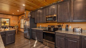 A modern kitchen with dark wood cabinets, stainless steel appliances, and a granite countertop. - Modern Cabin Movie Theater Hot Tub Game Room (Gatlinburg)