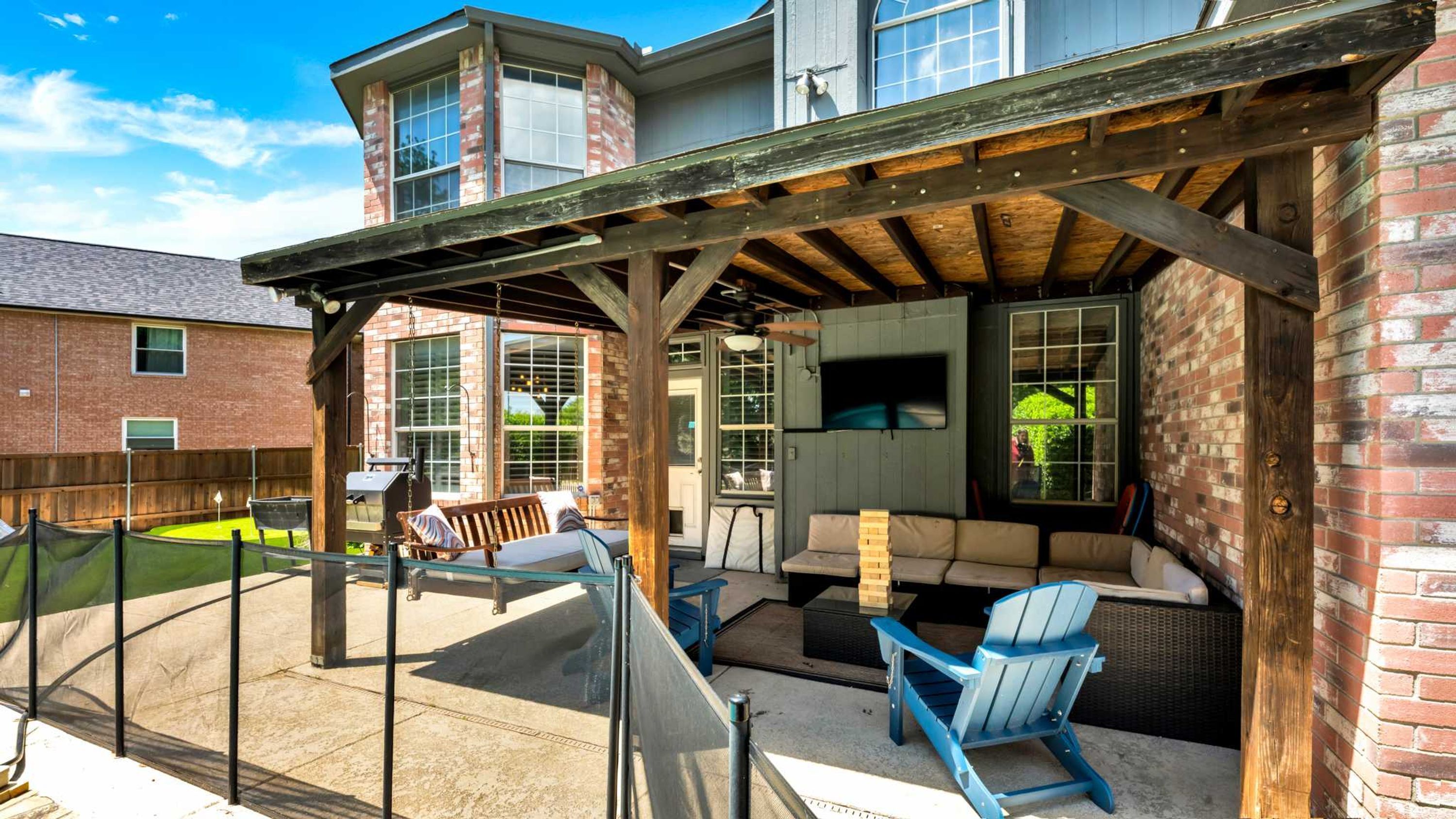 A covered patio with outdoor furniture, a grill, and a view of a brick building.