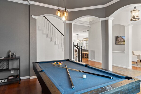 A pool table with pool cues and balls, a staircase, and a dining area with chairs and a table. - Heated Pool Hot Tub Sleeps 16 Putting Green (McKinney)
