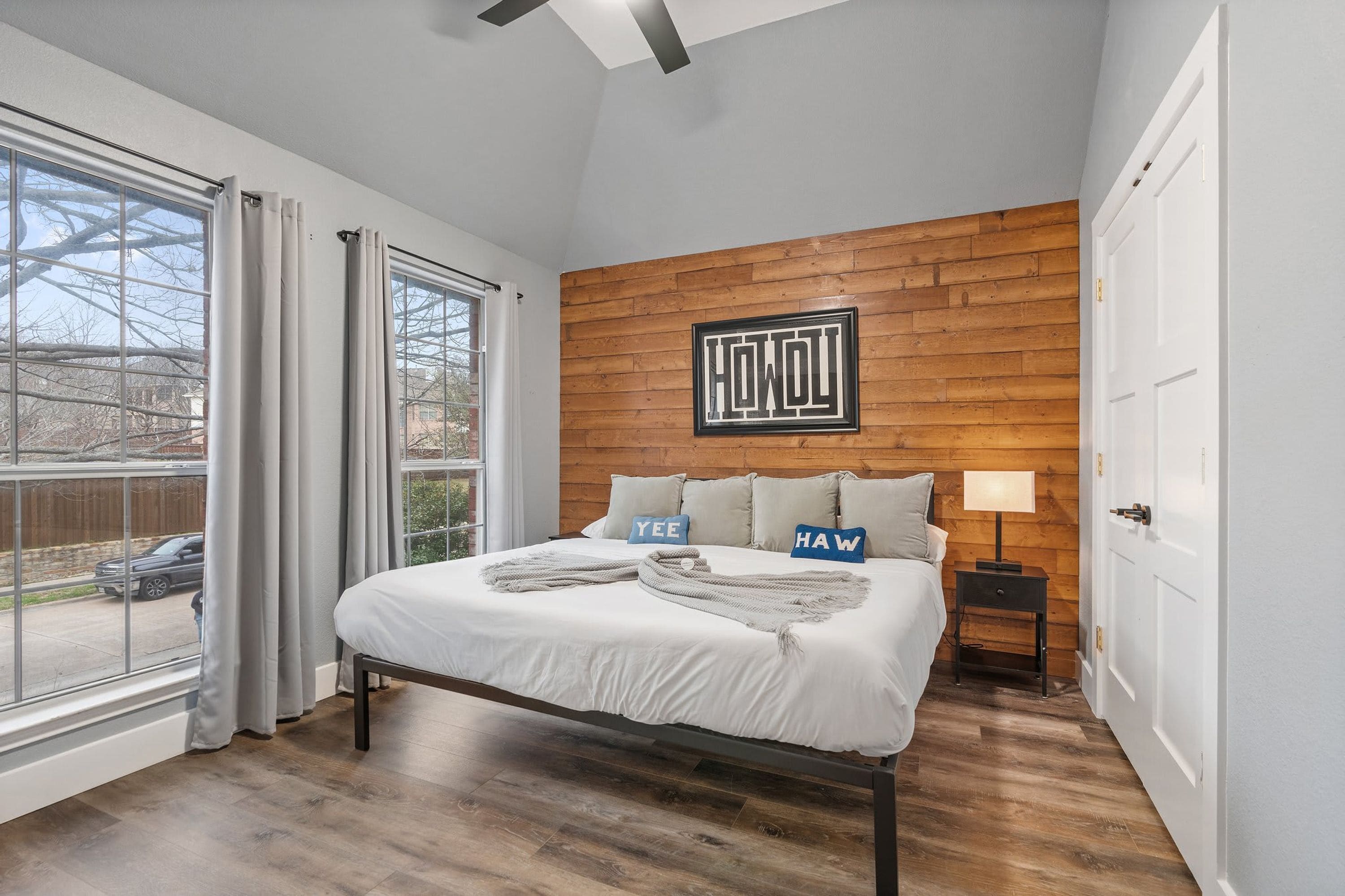 A bedroom with a bed, a wooden accent wall, a window, and a door.