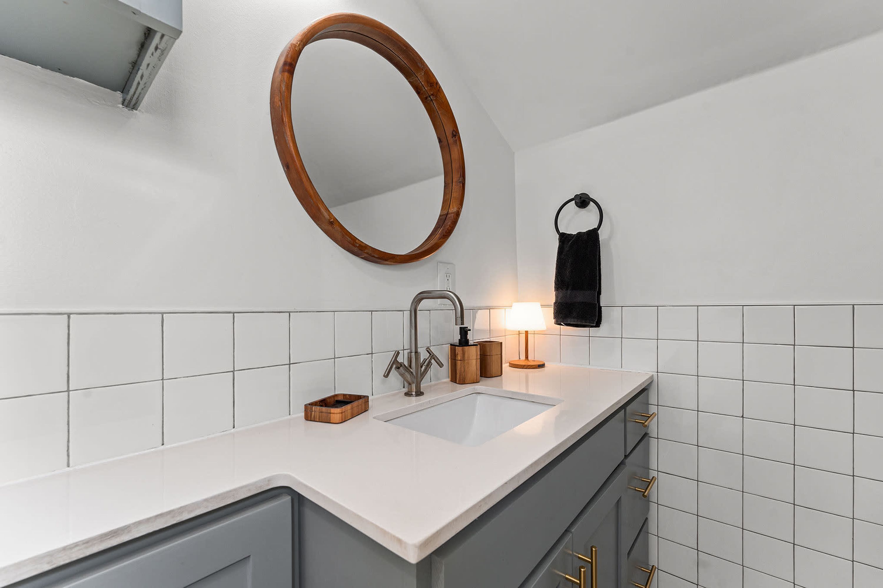Un baño moderno con un lavabo blanco, un espejo con marco de madera y un perchero para toallas.