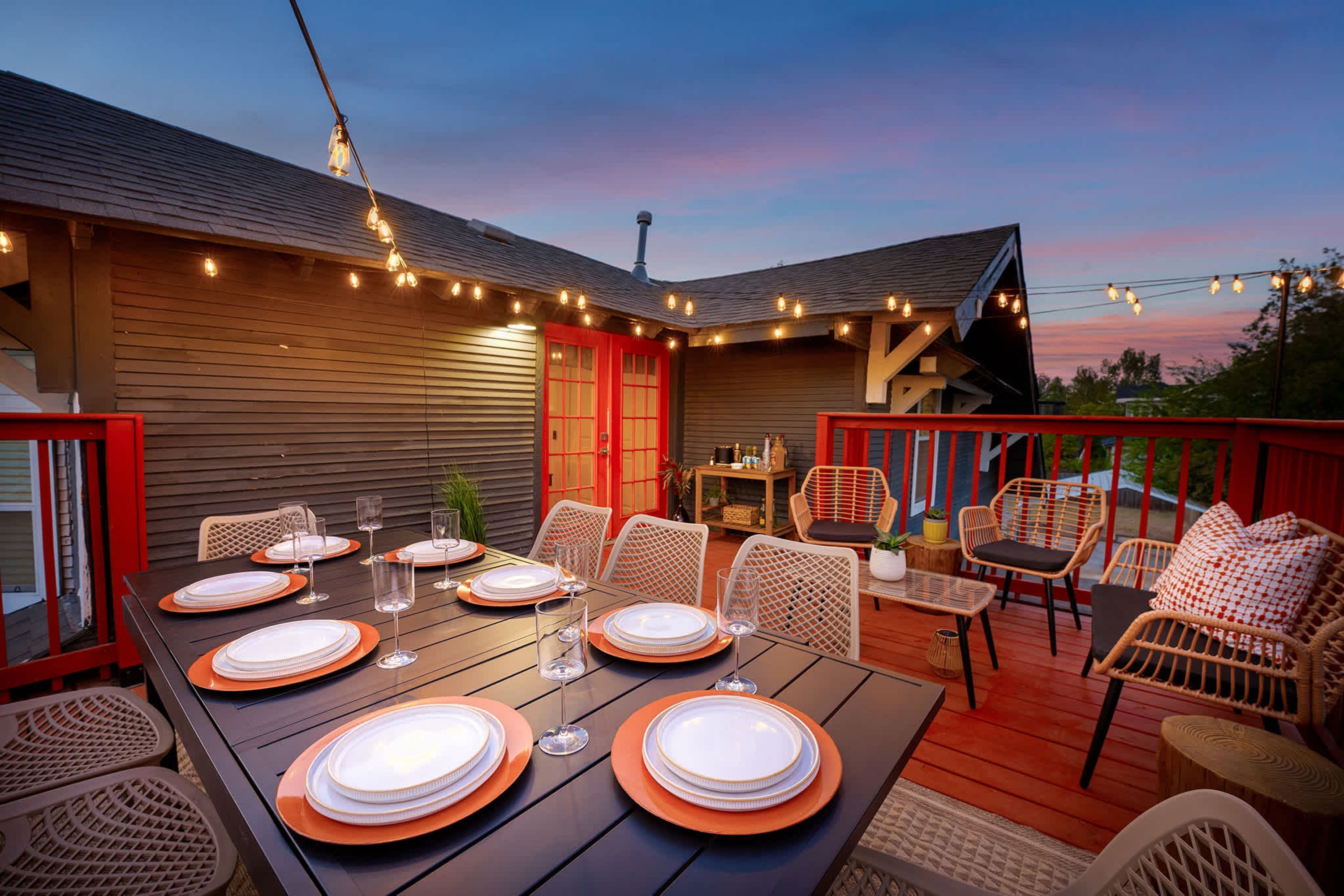 An outdoor dining area with a wooden deck, string lights, and wicker furniture.