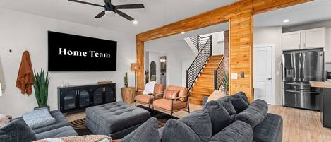 Ein modernes Wohnzimmer mit einem großen, grauen Ecksofa, einem Flachbildfernseher und einem Deckenventilator.