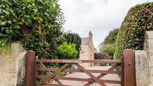 A wooden gate with a sign reading 'Prudhoe College' leading to a stone building with a pitched roof. - Prudhoe Cottage (Prudhoe)