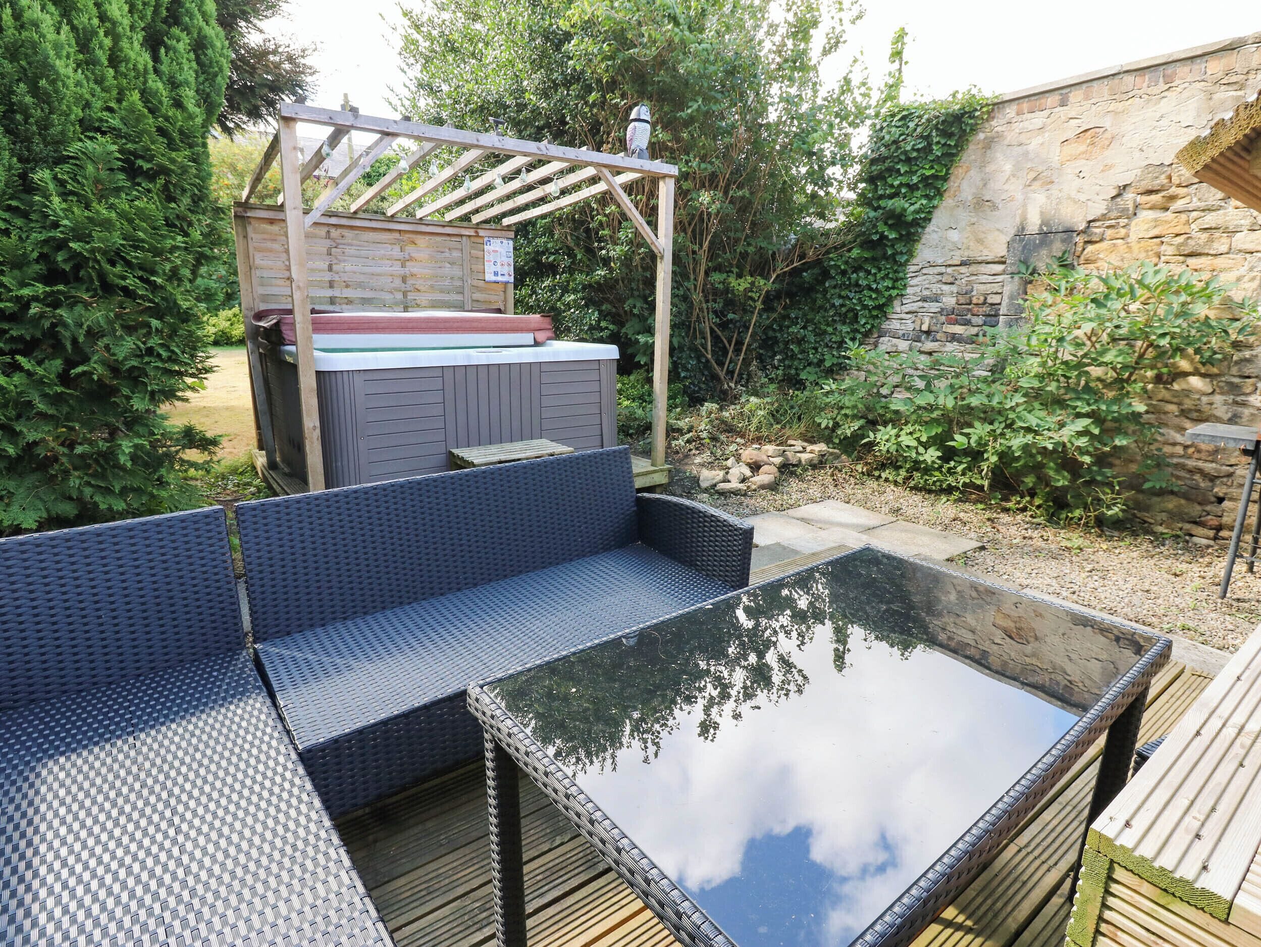 Un espace extérieur aménagé avec un coin salon, un jacuzzi, une terrasse en bois et un mur en pierre.