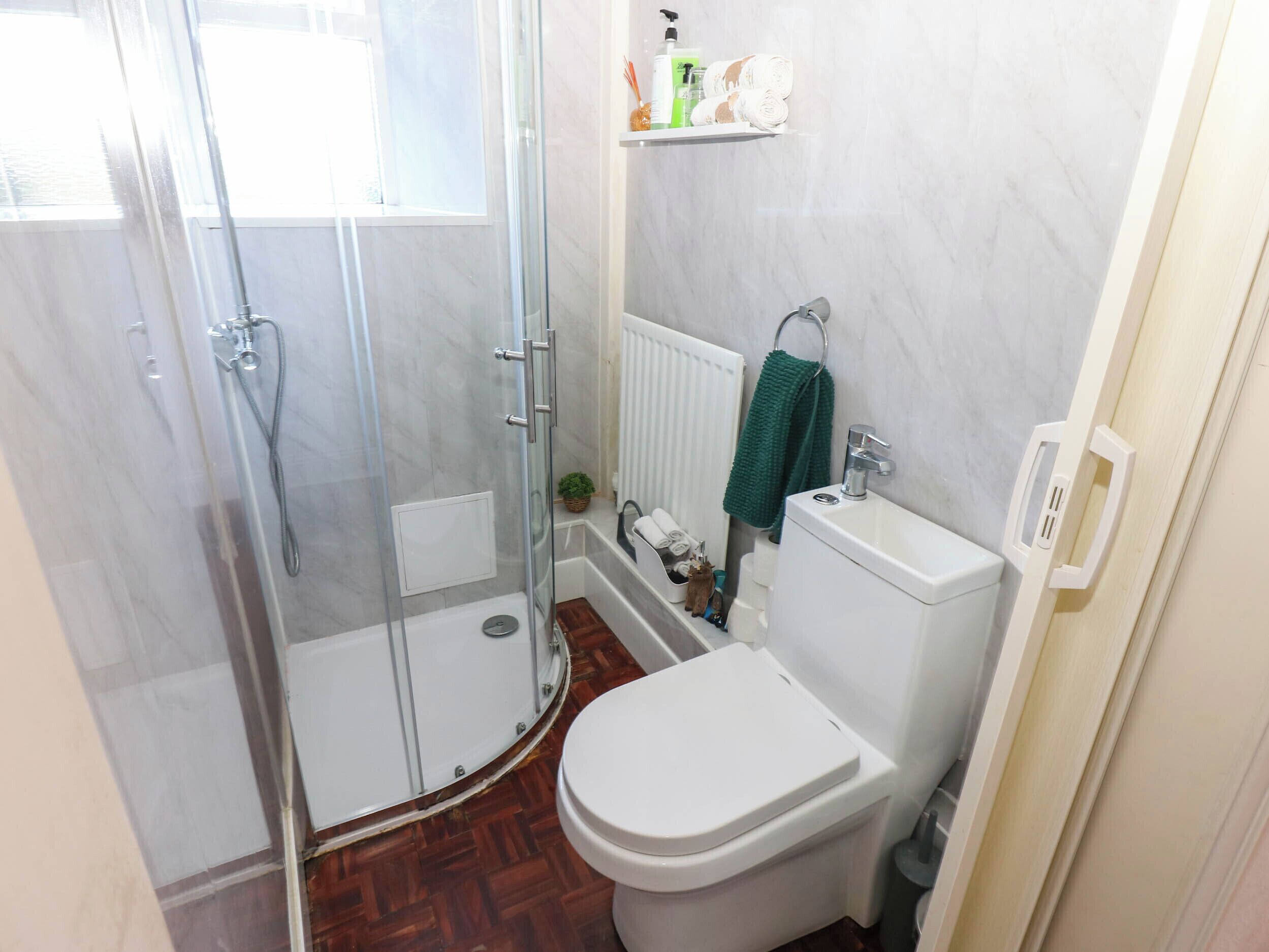 A bathroom with a glass shower enclosure, a toilet, a sink, and a radiator.