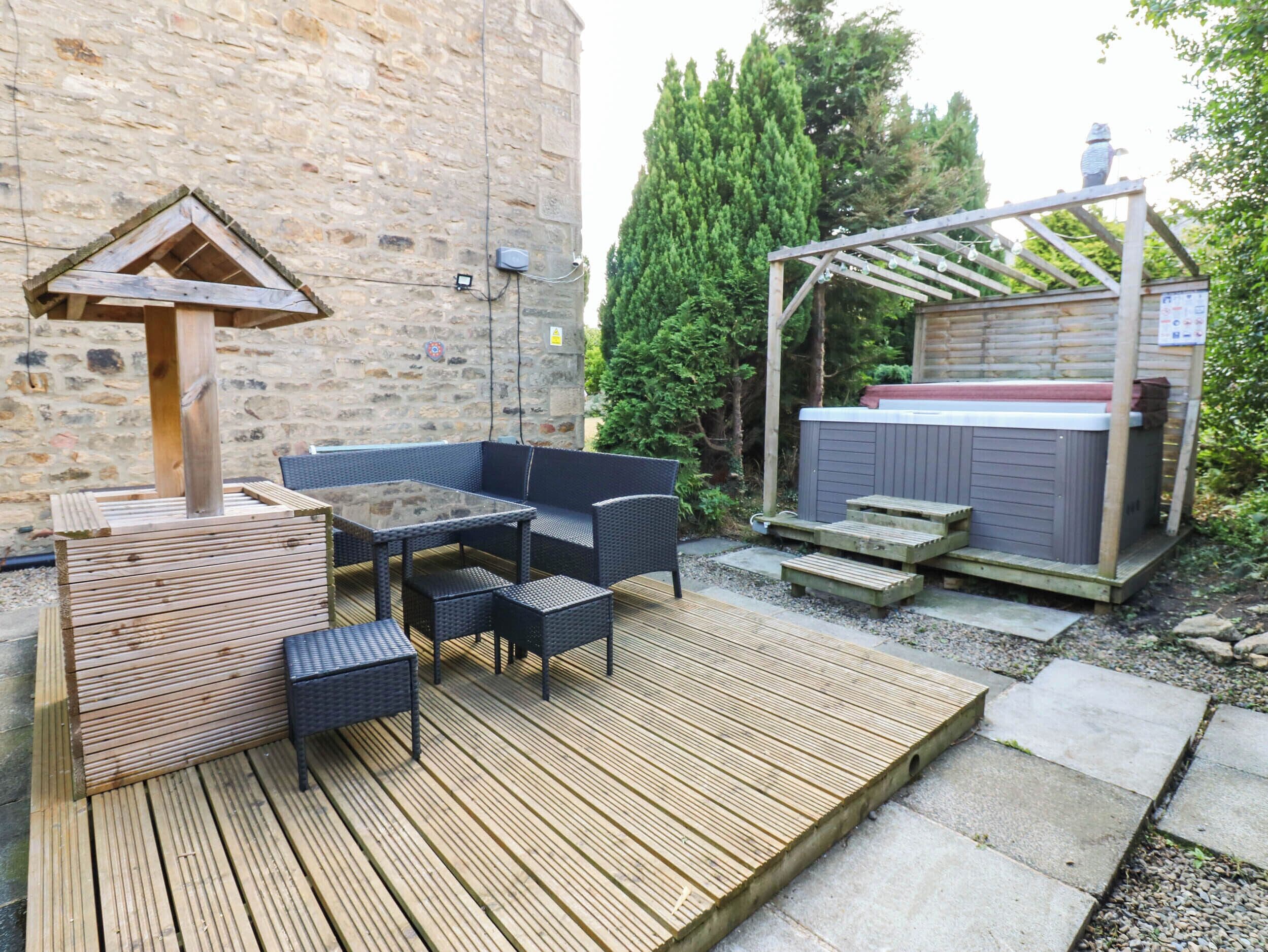 Un espacio al aire libre con un deck de madera, un conjunto de asientos y un jacuzzi.