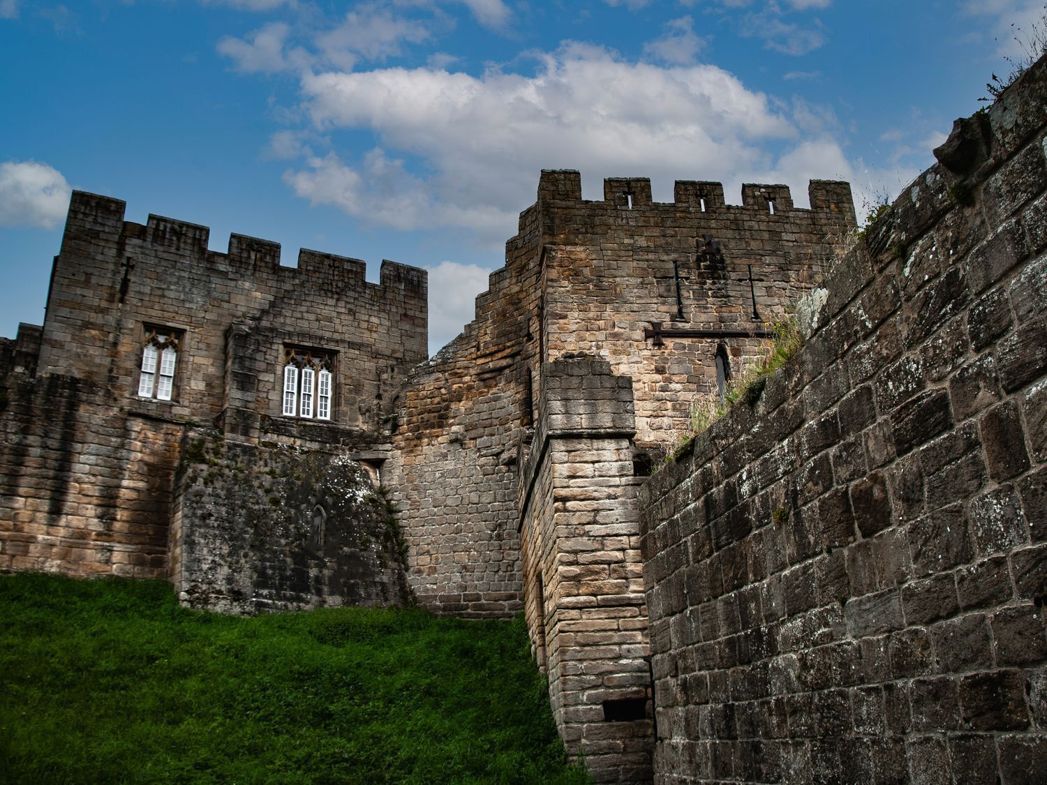 Eine historische Steinburg mit Zinnen, einem grasbewachsenen Vordergrund und einem teilweise bewölkten Himmel.