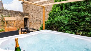 A hot tub with a bottle of champagne and glasses, surrounded by stone walls and greenery. - Prudhoe Cottage (Prudhoe)