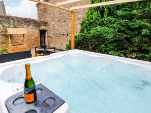 Ein Whirlpool mit einer Champagnerflasche und Gläsern, umgeben von Steinmauern und Grünpflanzen.