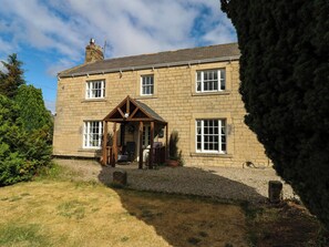 A stone building with a porch, a chimney, and a garden. - Prudhoe Cottage (Prudhoe)