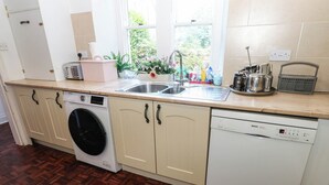 A kitchen with a washing machine, dishwasher, and a sink with a window above it. - Prudhoe Cottage (Prudhoe)