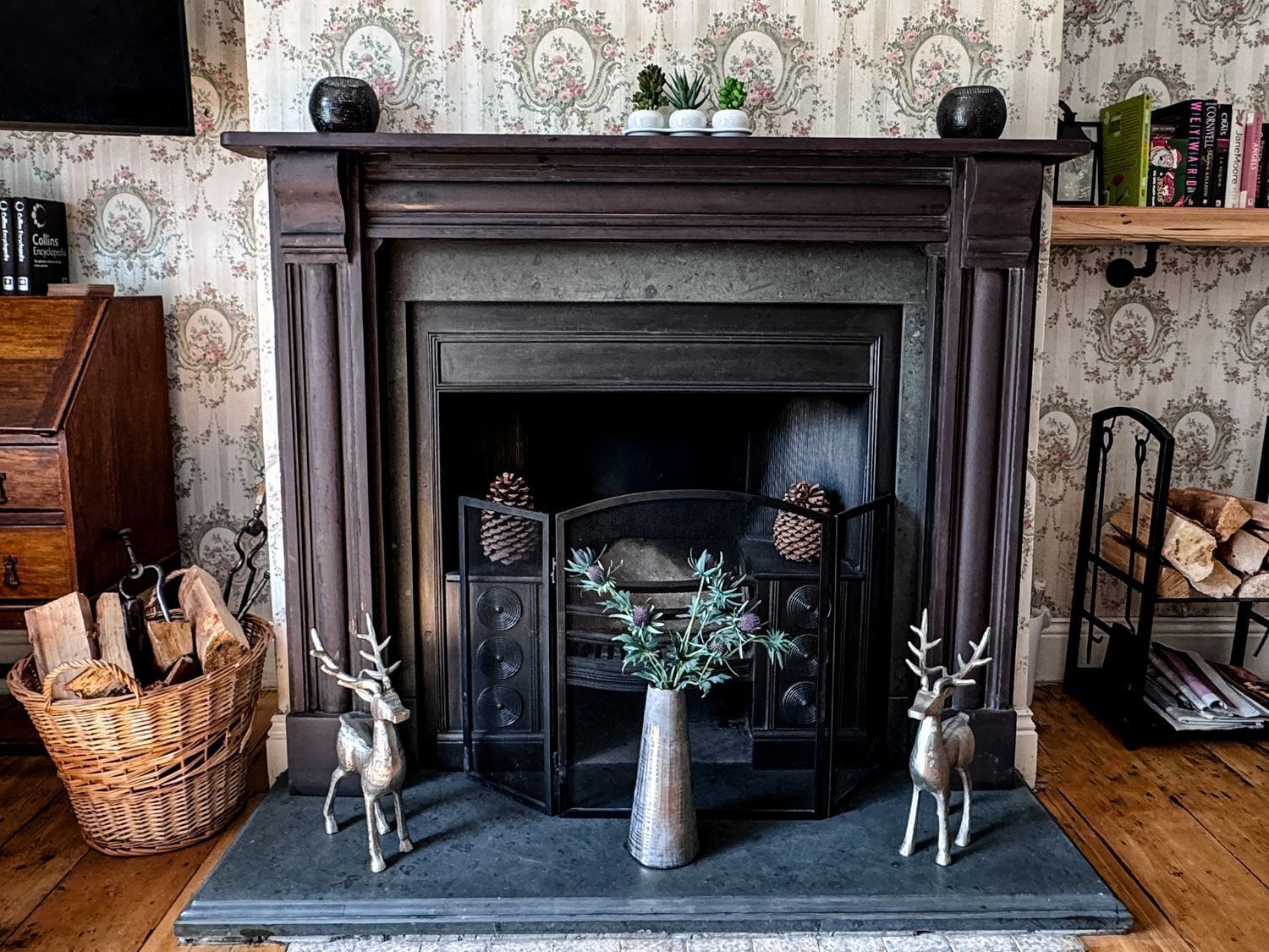 A fireplace with decorative items, a basket of firewood, and a bookshelf with books.