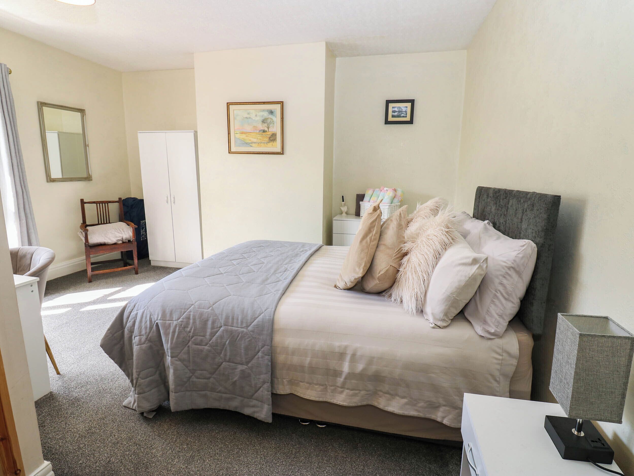 A bedroom with a bed, a chair, a wardrobe, and a nightstand with a lamp.