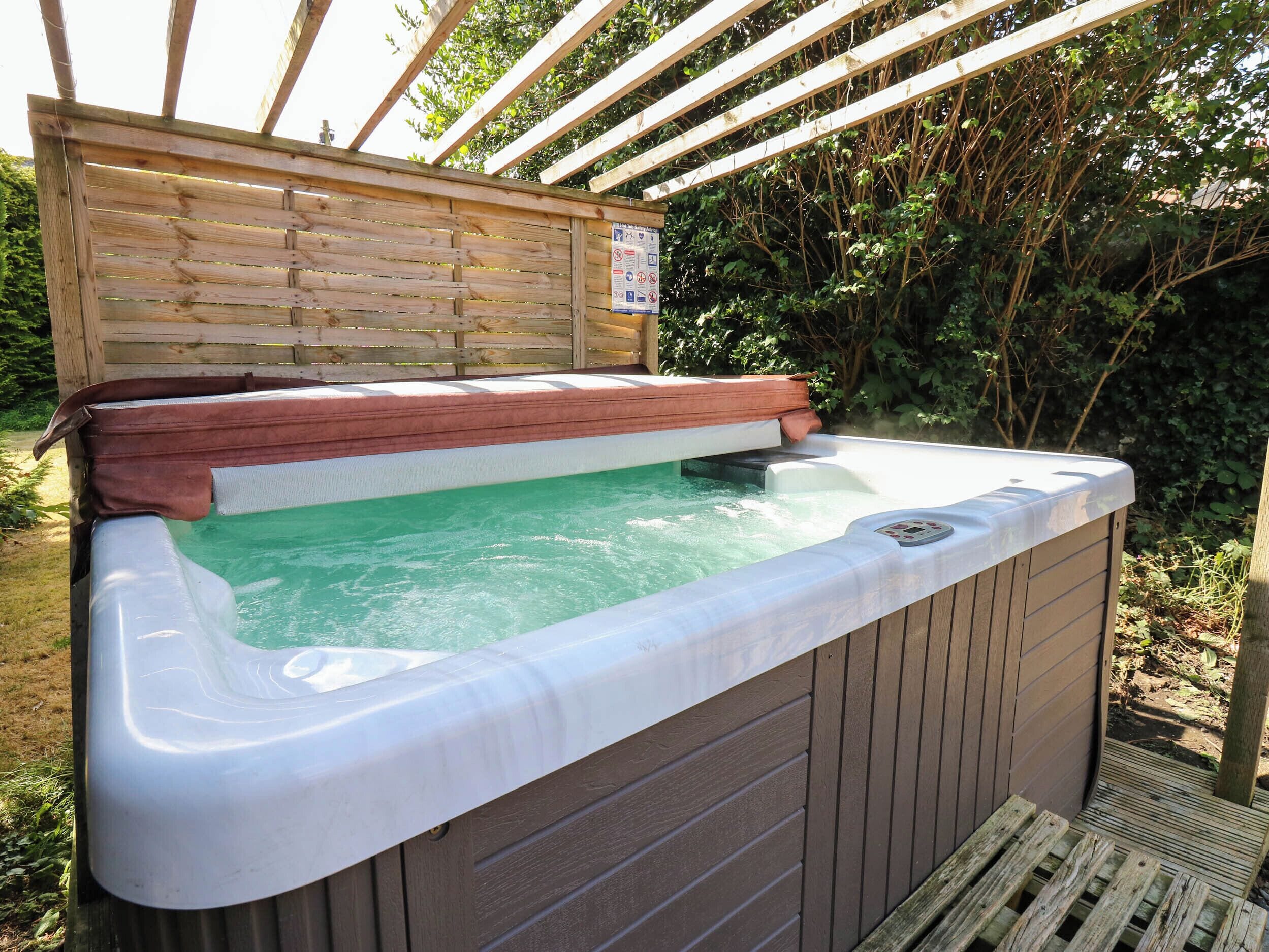 A hot tub with a wooden deck and a sign, surrounded by greenery.