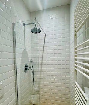 Eine Dusche mit Glastür, weißen Fliesen und einer Handbrause.
