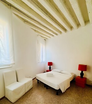 A bedroom with a bed, a chair, a window, and two bedside tables with lamps. - Apartment 'Ca Morosini Venezia' with Wi-Fi and Air Conditioning (Venice)