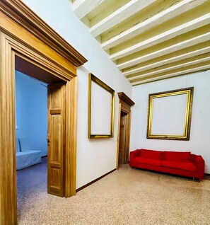 A room with a red sofa, wooden doors, and two framed pictures on the wall. - Apartment 'Ca Morosini Venezia' with Wi-Fi and Air Conditioning (Venice)