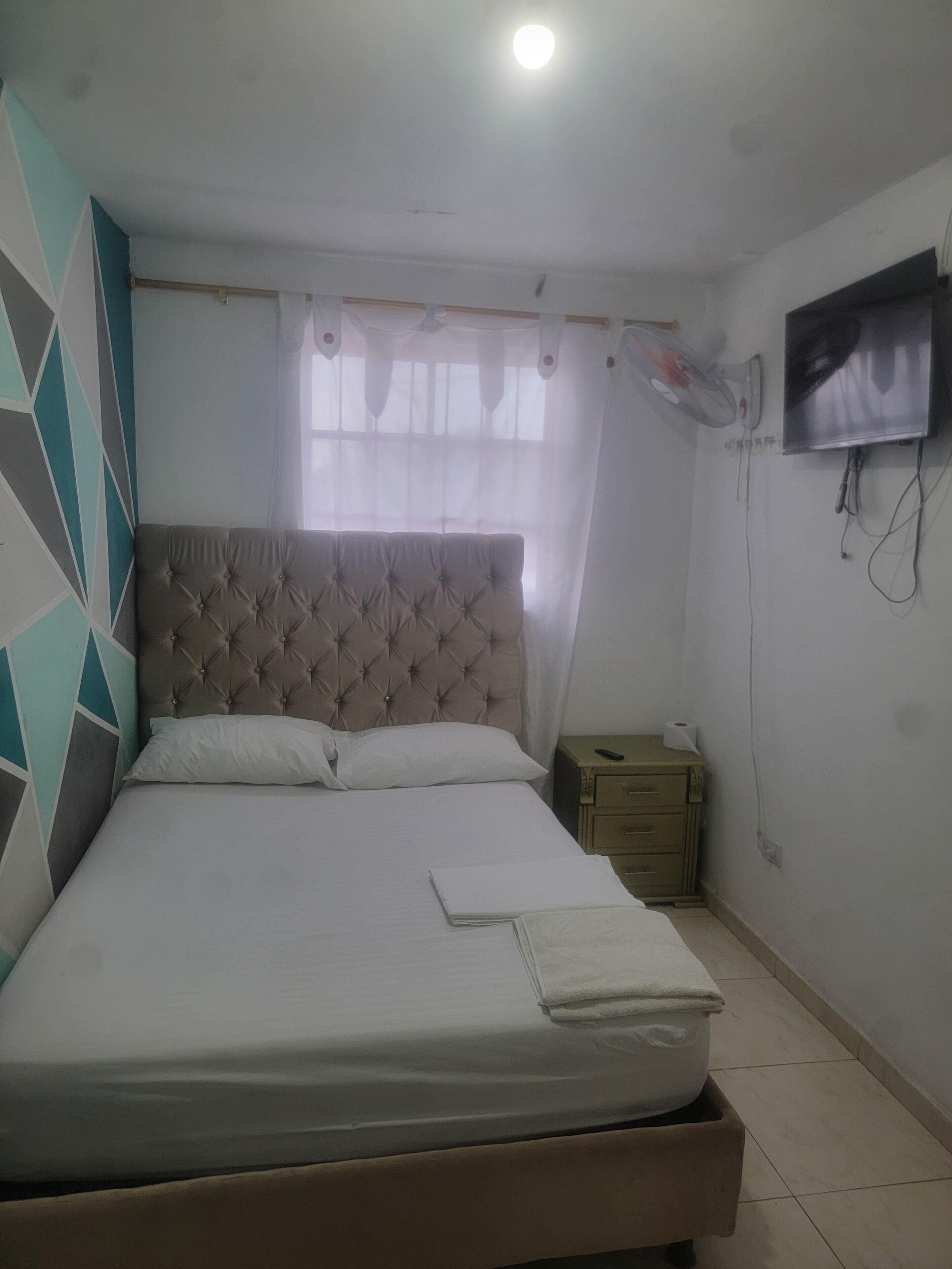 A bedroom with a bed, a nightstand, a TV, and a window with curtains.