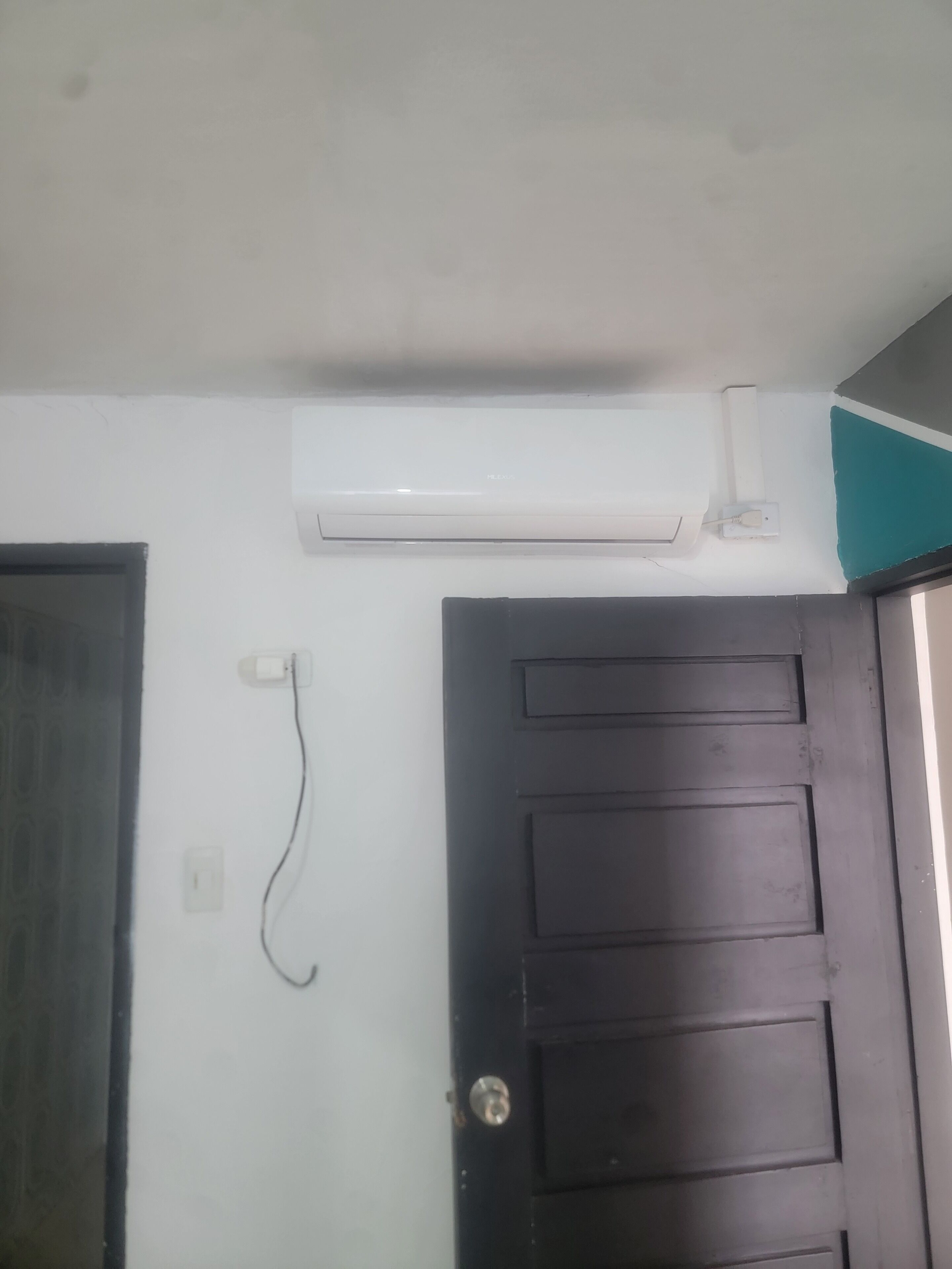 A room with a white ceiling, a black door, and an air conditioning unit mounted on the wall.