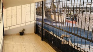 Una habitación con suelo de baldosas, una planta en maceta y una ventana con barrotes que da a una zona de piscina.