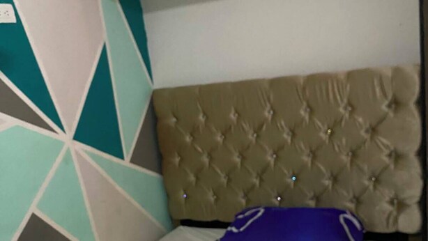 Una cama individual con cabecera capitonada, colchón blanco y almohada azul.