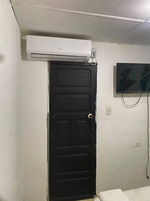 Una habitación con una puerta negra, un equipo de aire acondicionado montado encima y un televisor de pantalla plana en la pared.