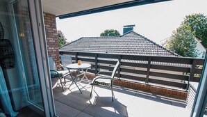 En glasdörr leder ut till en uteplats med ett bord och stolar, en mur av tegelsten och en takkonstruktion med takpannor.
