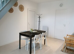 Een eethoek met een tafel, stoelen, een kapstok en een klok aan de muur.