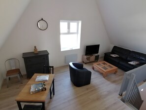 A modern living room with a wooden table, a black sofa, a television, and a window with blinds.