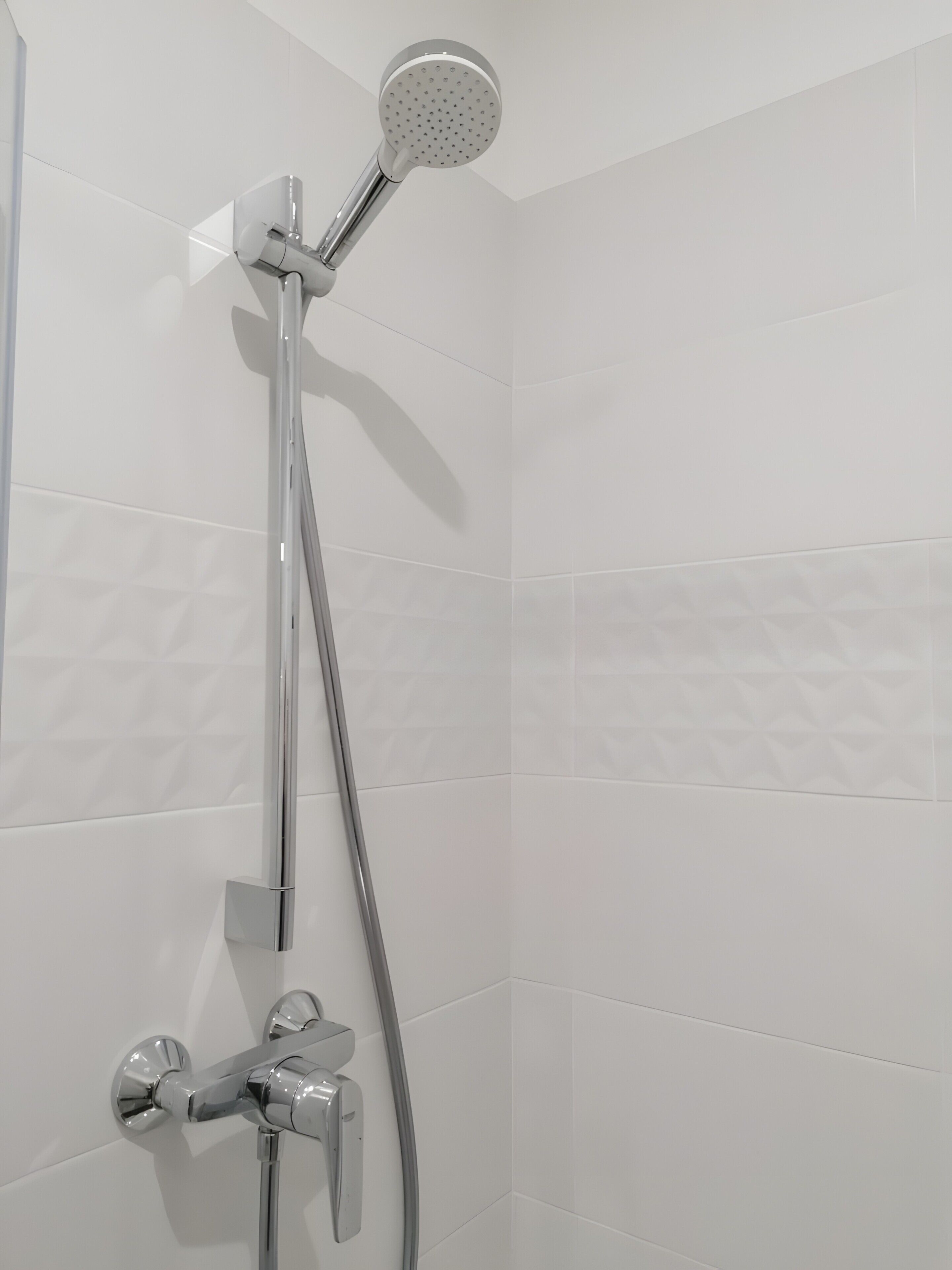 A shower with a handheld showerhead and a wall-mounted faucet.